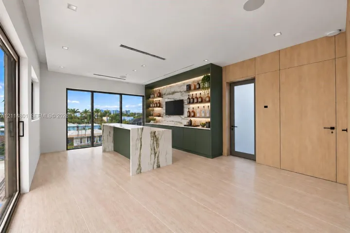 Custom wet bar featuring integrated stone-topped cabinetry, built-in shelving with recessed accent lighting, floor-to-ceiling wood paneling, wood-finish flooring, and expansive glass sliding doors