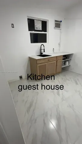 Cabinetry featuring light-toned wood finish, stone-surface countertop, rectangular basin with matte black pull-down faucet, and light-toned stone-finish tile flooring