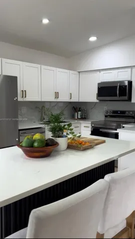 Kitchen featuring white shaker-style cabinetry, quartz countertops, a stone-patterned backsplash, stainless steel appliances, and a central island with a slatted base