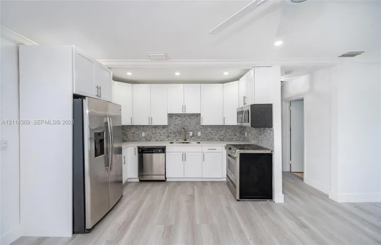 Kitchen featuring white shaker-style cabinetry, stainless steel appliances, a mosaic tile backsplash, wood-finish flooring, and recessed ceiling lighting