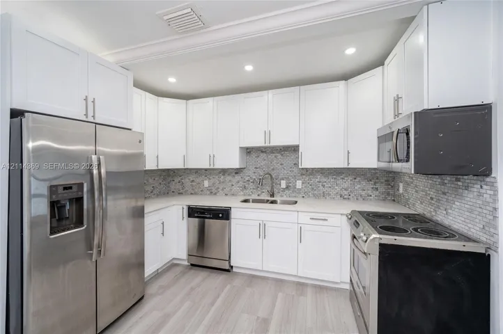 Kitchen featuring white cabinetry, stainless steel appliances, neutral stone-finish countertops, mosaic tile backsplash, and light-toned wood-finish flooring