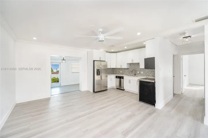 Kitchen featuring white cabinetry, stainless steel appliances, patterned stone-style backsplash, wood-finish flooring, and a ceiling fan