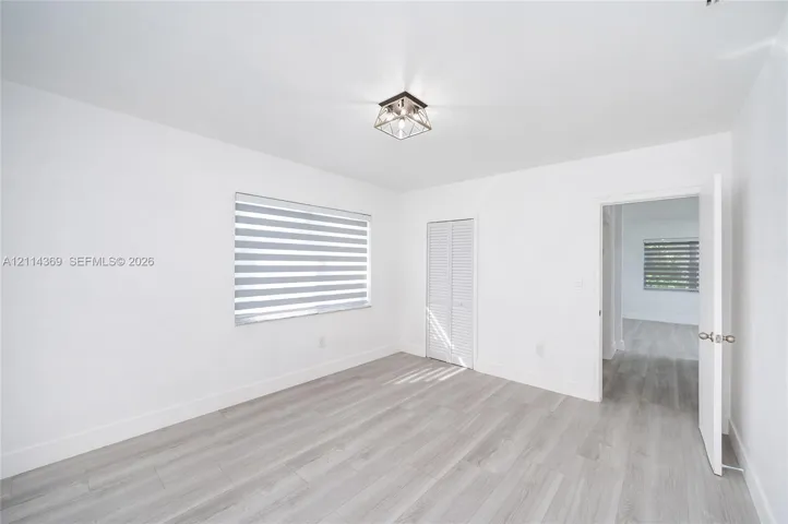 Wood-finish flooring, geometric ceiling light fixture, louvered-style closet doors, and adjustable dual-layer window shades