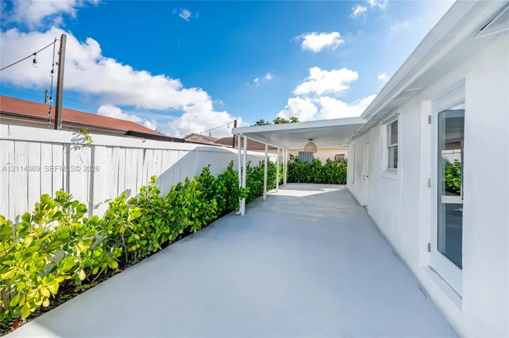 Covered concrete patio featuring a white pergola structure, perimeter privacy fencing, and established hedge landscaping