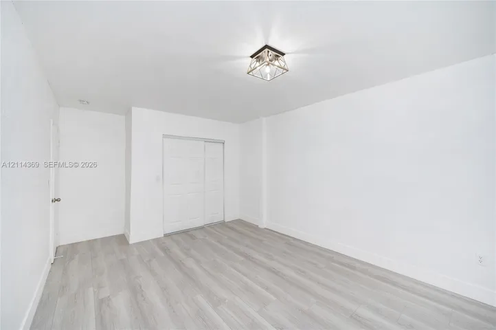 Room featuring wood-finish flooring, white walls, a dual-panel sliding closet door, and a geometric metal-frame flush-mount light fixture