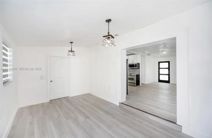 Interior featuring wood-finish flooring, geometric pendant lighting, modern paneled door, and kitchen with stainless steel appliances