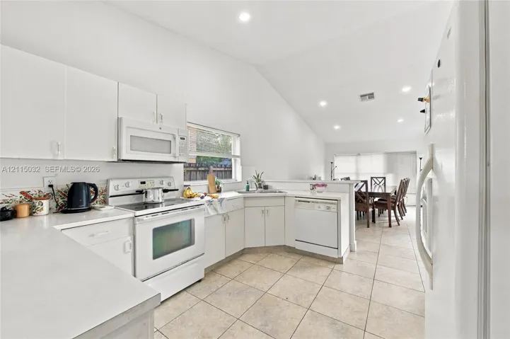 Kitchen featuring white cabinetry, solid-surface countertops, tile flooring, recessed lighting, and a vaulted ceiling