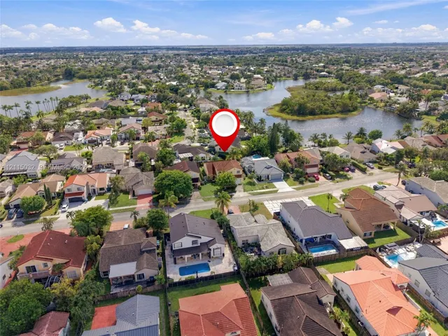 Aerial perspective featuring a residential property situated on a lot with mature landscaping and proximity to a community lake