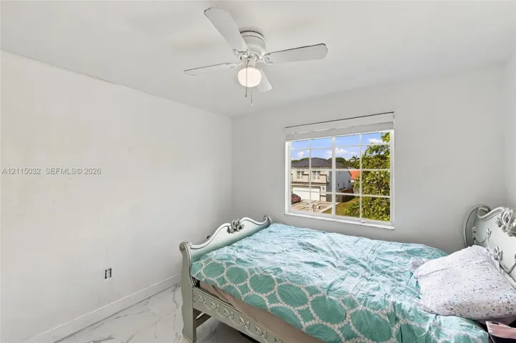 Neutral-toned room featuring stone-finish flooring, a white ceiling fan with integrated lighting, and a multi-pane grid window