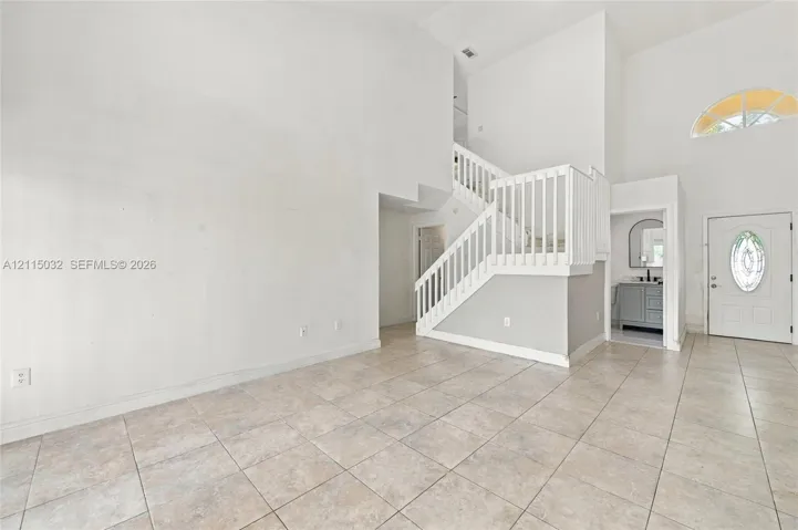 Vaulted ceilings, tile flooring, staircase with white railing, and entryway door with decorative glass inlay