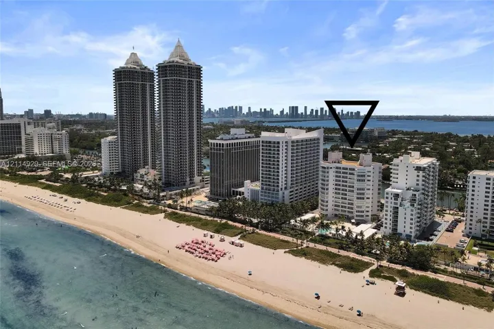 High-rise building featuring a white facade, direct beach frontage, and a pool area with mature palm trees