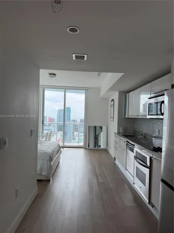 Kitchen featuring high-gloss cabinetry, stone countertops, stainless steel appliances, and wood-finish flooring, accompanied by floor-to-ceiling glass sliding doors