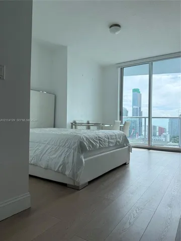 Floor-to-ceiling windows featuring urban skyline scenery, wood-finish flooring, and a glass-paneled balcony