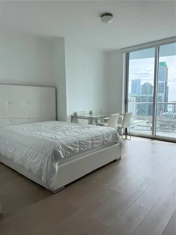 Floor-to-ceiling windows, wood-finish flooring, and a glass-paneled balcony door with urban skyline scenery