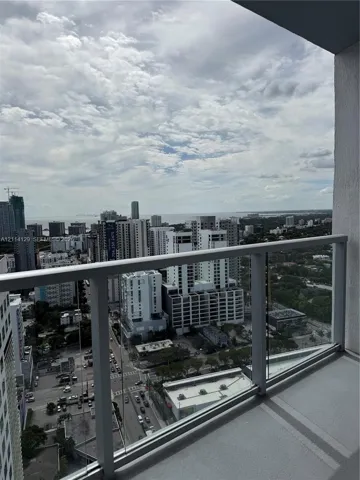 Covered balcony with a glass panel railing, offering expansive urban and coastal horizons