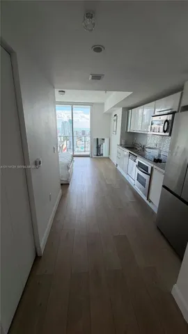 Kitchen featuring high-gloss cabinetry, stone countertops, stainless steel appliances, wood-finish flooring, and floor-to-ceiling glass sliding doors