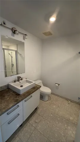 Bathroom featuring a floating vanity with a square vessel sink, stone-surface countertop, tile flooring, and a glass-enclosed shower