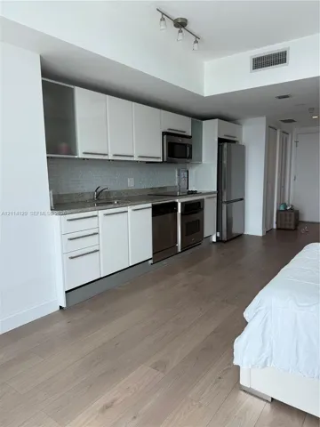 Kitchen featuring white cabinetry, stone-finish countertops, subway tile backsplash, and stainless steel appliances, complemented by wood-finish flooring
