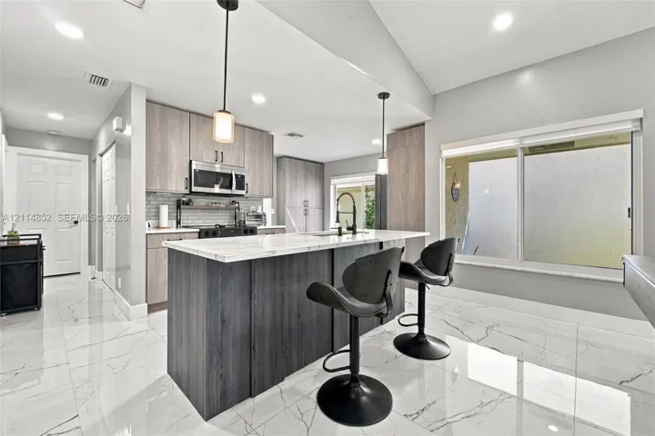 Kitchen featuring wood-finish cabinetry, a central island with a stone-top surface, large-format tile flooring, recessed lighting, and dual pendant light fixtures