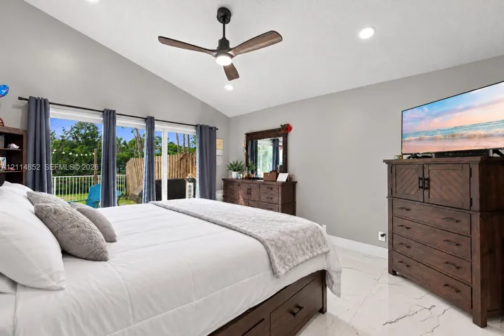 Vaulted ceiling with a matte black modern ceiling fan, large glass sliding doors, and polished stone-finish flooring