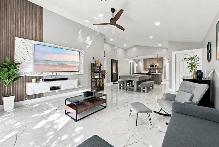 Open-concept living space featuring high vaulted ceilings, large-format polished tile flooring, a vertical wood-slat accent wall, and a custom wall-mounted floating media console with stone-finish cladding