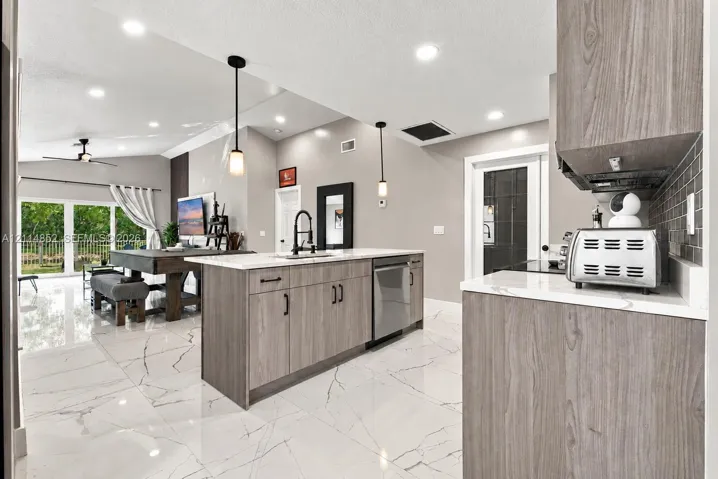 Kitchen featuring wood-finish cabinetry, stone-style countertops, recessed ceiling lighting, pendant light fixtures, and large-format tile flooring