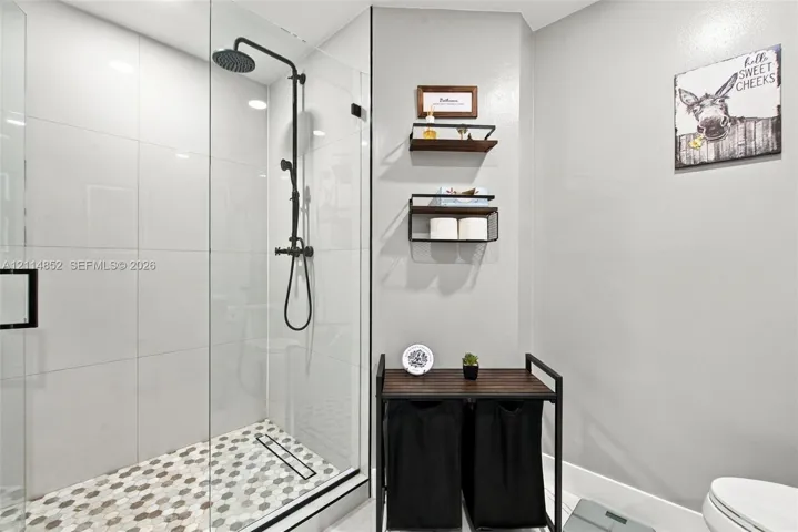 Walk-in shower featuring a frameless glass enclosure, matte black rainfall showerhead, and hexagonal mosaic floor tile