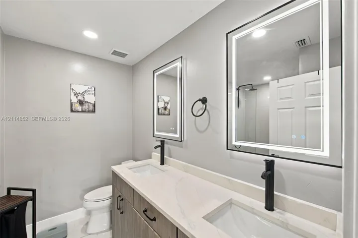 Double vanity featuring a light-toned countertop, dual rectangular undermount sinks, matte black tall-spout faucets, and rectangular backlit mirrors