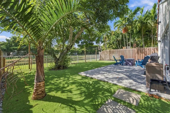 Private backyard featuring a paved stone patio, synthetic turf lawn, mature palm trees, and perimeter wood fencing