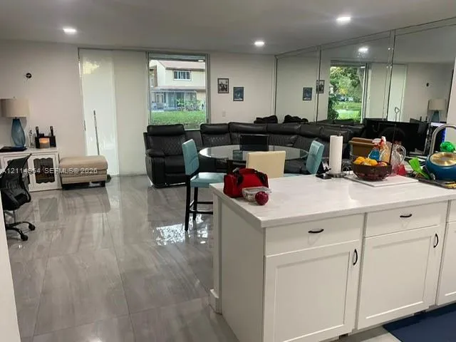 Open floor plan featuring large-format porcelain tile flooring, recessed lighting, mirrored wall accents, and white cabinetry topped with stone-finish surfaces
