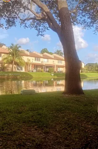 Waterfront property featuring a canal, mature trees, manicured lawn, and multi-unit residential structures