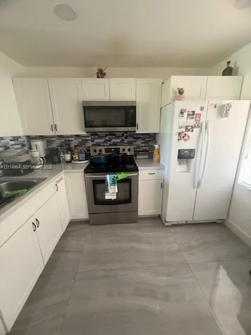 Kitchen featuring white shaker-style cabinetry, stainless steel appliances, a multi-tone tile backsplash, and large-format gray flooring tiles