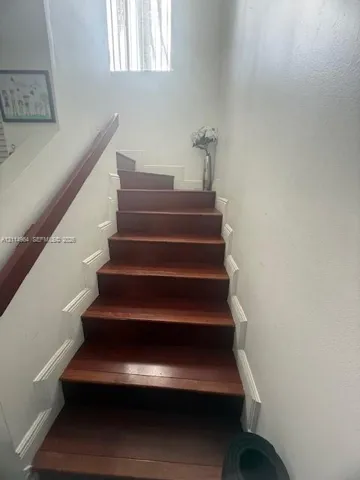 Staircase featuring wood-finish treads, white risers, decorative millwork, and a wall-mounted wooden handrail