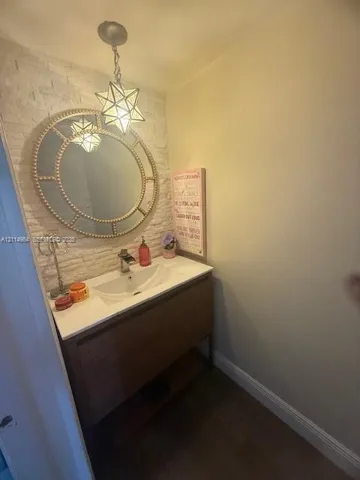 Vanity featuring a wood-finish cabinet with an integrated white sink, textured stone accent wall, decorative circular wall-mounted mirror, and geometric pendant lighting