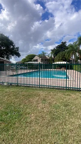 In-ground swimming pool featuring a surrounding paver deck, metal perimeter fencing, and covered cabana structures