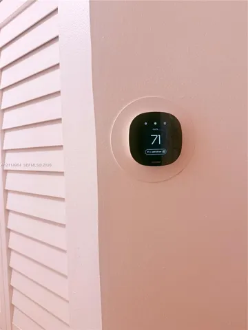 Smart digital thermostat with a touch-screen interface, mounted on a wall with integrated louvered cabinetry