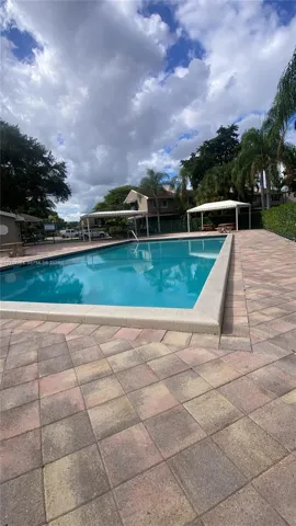 Rectangular swimming pool featuring a concrete coping border, paver stone pool deck, and two covered cabanas