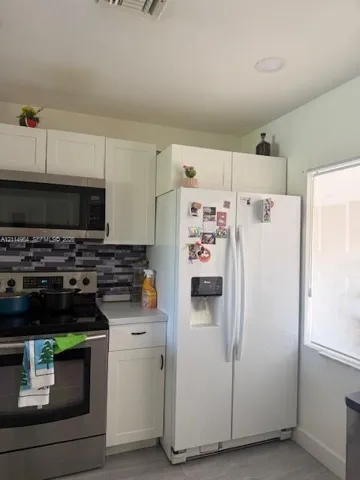 Kitchen featuring white shaker-style cabinetry, mosaic tile backsplash, stainless steel microwave, and wood-finish flooring
