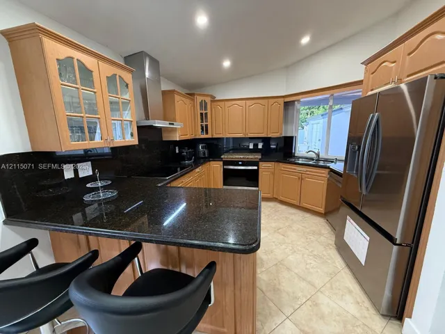 Kitchen featuring wood cabinetry, stone countertops, stainless steel appliances, recessed ceiling lighting, and tile flooring