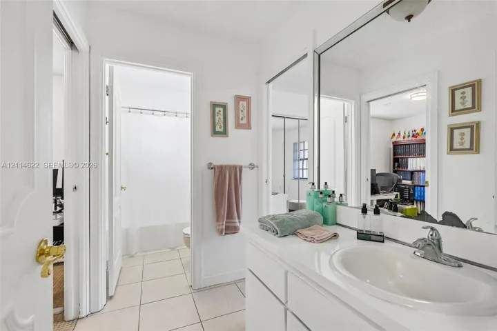 Bathroom featuring a white vanity cabinet, integrated sink with a polished chrome faucet, large wall-mounted mirror, and tile flooring