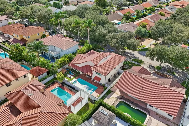 Aerial perspective showcasing properties with terracotta-style tile roofing, in-ground swimming pools, and enclosed backyard spaces featuring mature palm trees and established landscaping