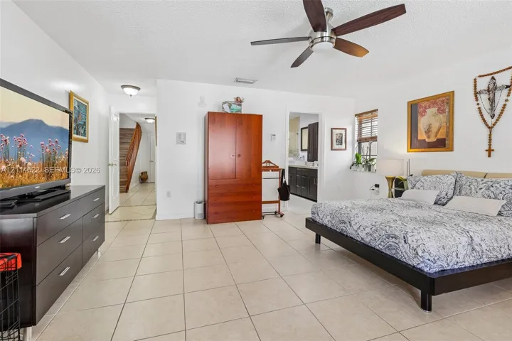 Spacious room featuring neutral ceramic tile flooring, a multi-blade ceiling fan, and blinds covering the window
