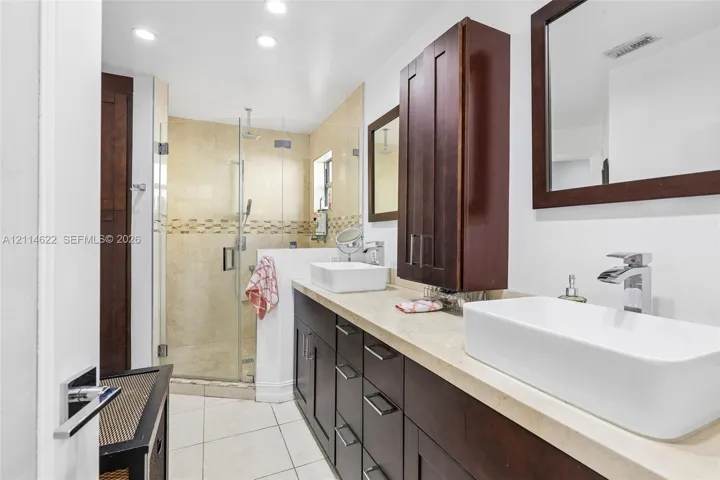 Dual vanity featuring dark wood-finish cabinetry, stone-style countertops, rectangular vessel sinks, and frameless glass shower enclosure