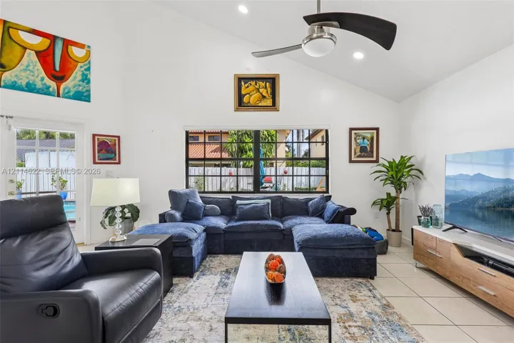 Vaulted ceiling featuring a central multi-blade ceiling fan, expansive multi-pane window, and light-toned tile flooring