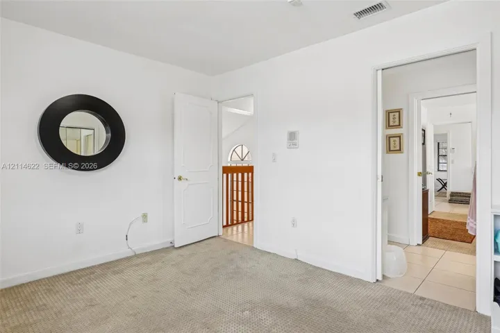 Room interior featuring wall-to-wall carpeting, a circular wall-mounted mirror, white panel doors, and a wood-slat interior railing