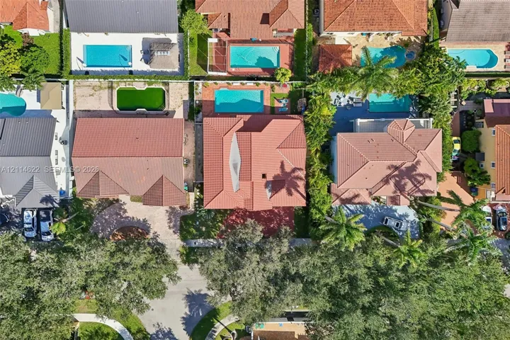 Aerial perspective of a multi-hip tile roof, private swimming pool, concrete paved driveway, and established canopy trees
