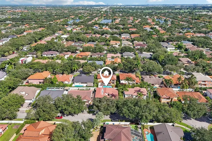 Aerial perspective of a multi-story residence featuring a tile roof, an in-ground swimming pool, and mature landscaping within a tree-lined residential community