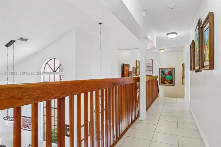 Hallway featuring light-colored tile flooring, a vaulted ceiling, natural wood balustrades, arched windows, and recessed lighting