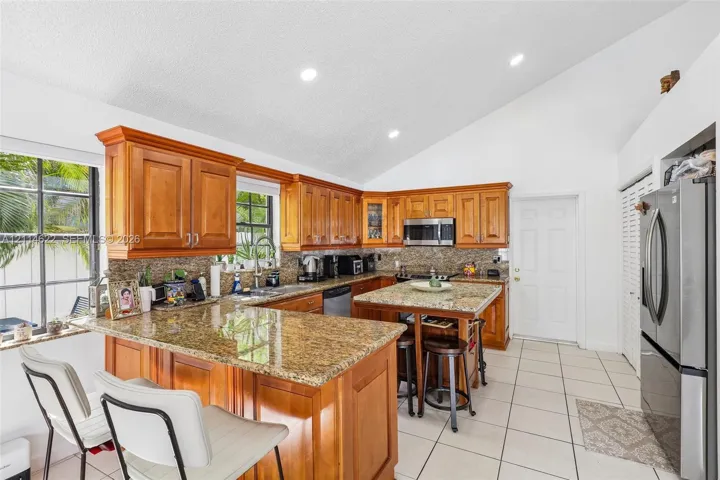 Kitchen featuring vaulted ceilings, natural wood cabinetry, stone-surfaced countertops, a center island with built-in seating space, and tile flooring
