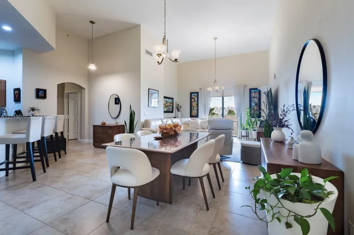 Open-concept area featuring high vaulted ceilings, large-format tile flooring, a built-in kitchen breakfast bar with pendant lighting, and multi-light chandeliers